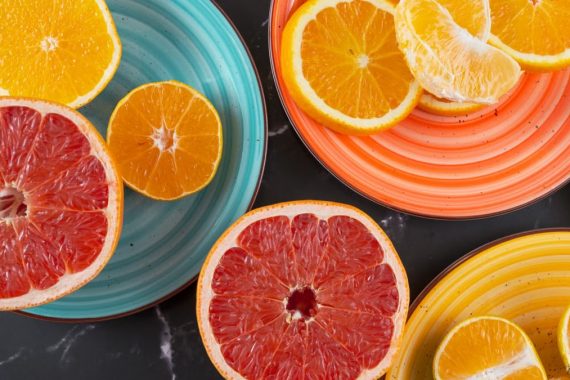 Top view of sliced citrus fruits on multicolored plates, featuring oranges, grapefruit, and mandarins.