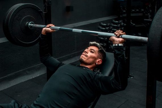 Man performing bench press with heavy barbell in a gym setting, focusing on strength training.
